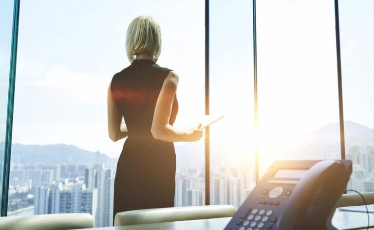 Woman standing in an office with a city view, holding a tablet
