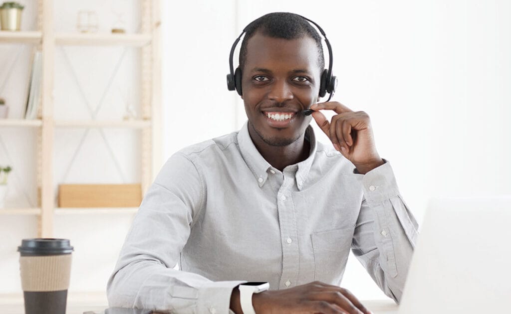 Man with a headset smiling while working at a laptop