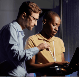 Two IT professionals working on a laptop in a server room environment